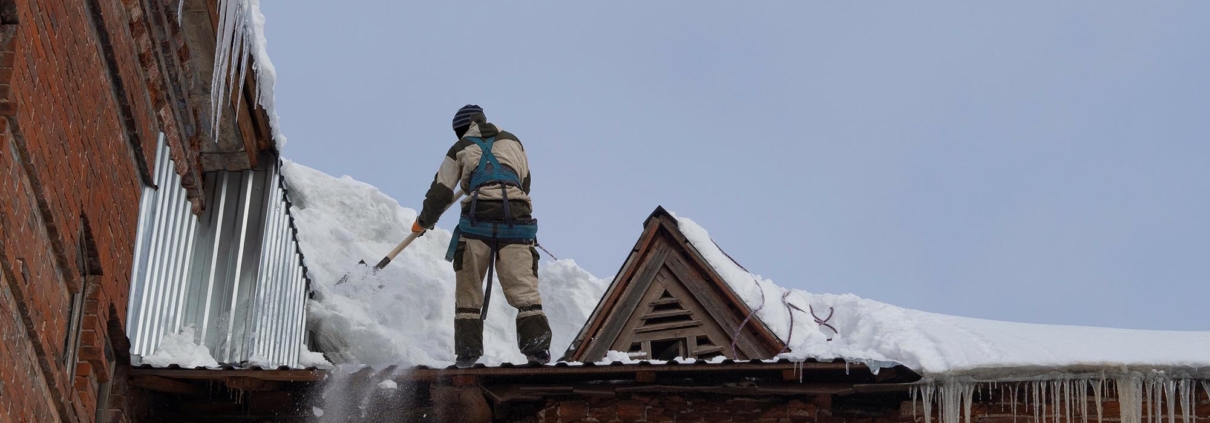 Worm's eye view of a man standing on a commercial roof cleaning snow off with a shovel